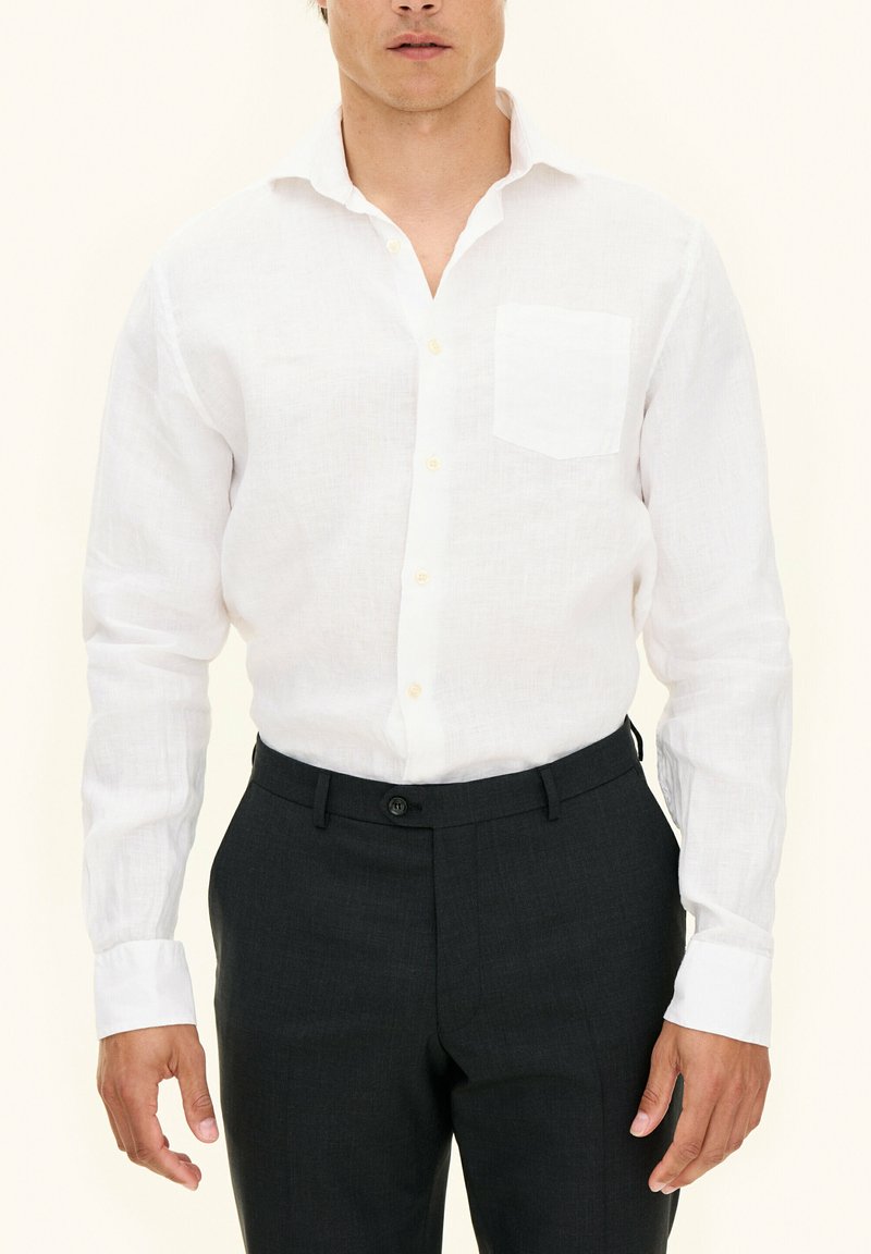 Witte linnen shirt met een borstzak, manchetten met knopen en lichte knopen, gecombineerd met donkere op maat gemaakte broek. Glad stoffen textuur.