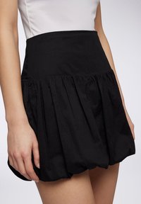 Gonna nera con vita aderente, caratterizzata da pieghe che creano una silhouette svasata. Realizzata in tessuto leggero con una texture liscia.