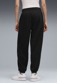 Sorte bomuldsjoggers med elastisk talje og manchetter. Bæres med hvide sneakers med blå og rød stribe på siden.