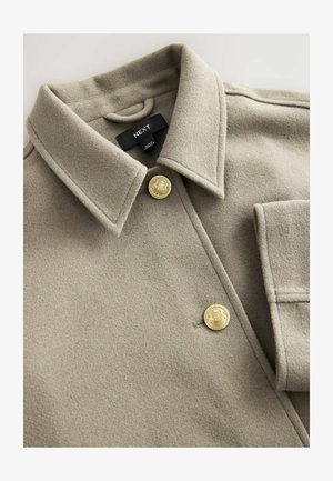 Bežinė vilnonė striukė su klasikinio tipo apykakle, dviem auksinėmis sagomis ir kišene. Švelni tekstūra su matomais siuvimo detalėmis. Prekės ženklo etiketė viduje.