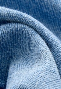 Tissu bleu clair avec une surface texturée, présentant un motif de tissage doux et des variations de couleur subtiles. Idéal pour des vêtements décontractés.