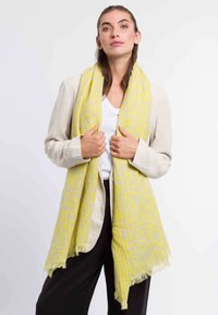 Gelber gemusterter Schal mit fransigen Kanten, aus leichtem Stoff, �über einem lässigen Outfit drapiert. Verfügt über komplexe geometrische Designs.