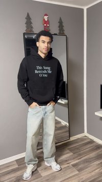 Crna dukserica s natpisom "Ova pjesma me podsjeća na tebe," svijetloplavo slovo, uparena sa svijetlim trapericama i bijelim tenisicama.