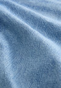 Világoskék farmeranyag lágy tapintással, finom halszálkás mintázattal és sima felülettel. Az anyag enyhén gyűrődöttnek tűnik.