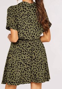 Kortærmet kjole i olivengrønt stof med sort leopardprint. Flared design, taljebånd og plissert nederdel for bevægelse.