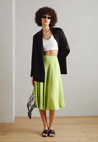 Svart blazer, hvit crop top og en limegrønn midikjole. Svarte sandaler og en mønstret håndveske. Glatte teksturer, tettsittende og flytende elementer.
