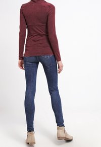 Bordeaux långärmad topp med en figurnära design, kombinerad med mörkblå skinny jeans och beige ankelstövlar med detaljer av sidoglider.