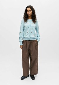 Cardigan bleu clair avec broderie florale, associé à un pantalon large marron et des chaussures noires. Le cardigan est boutonné à l'avant.