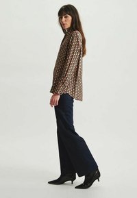 Blouse à manches longues avec un motif géométrique multicolore, dotée d'un col montant. Associée à un jean flare bleu marine et des escarpins noirs à bout pointu.