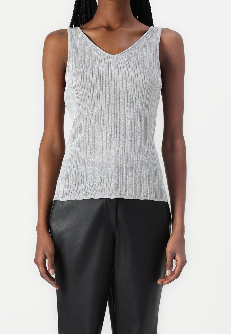 Top senza maniche di colore argento a coste con scollo a V; texture leggera; abbinato a pantaloni in pelle neri.