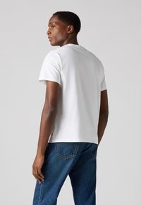 Witte katoenen T-shirt met korte mouwen, ronde halslijn en een normale pasvorm. Gestyled met blauwe denim jeans, met een achteraanzicht en stoftextuur.