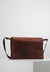 Borsa messenger in pelle marrone con design piatto, dotata di un copri sopra pieghevole e di una robusta tracolla regolabile. Texture liscia con cuciture sottili.