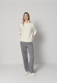White knit sweater with a high neckline, paired with gray pinstripe trousers and white sneakers. Simple, relaxed fit.