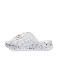 Witte slip-on sandaal met een geperforeerde bovenkant, voorzien van een decoratieve band en een gespikkelde witte en grijze zool. De hele sandaal heeft een gladde textuur.