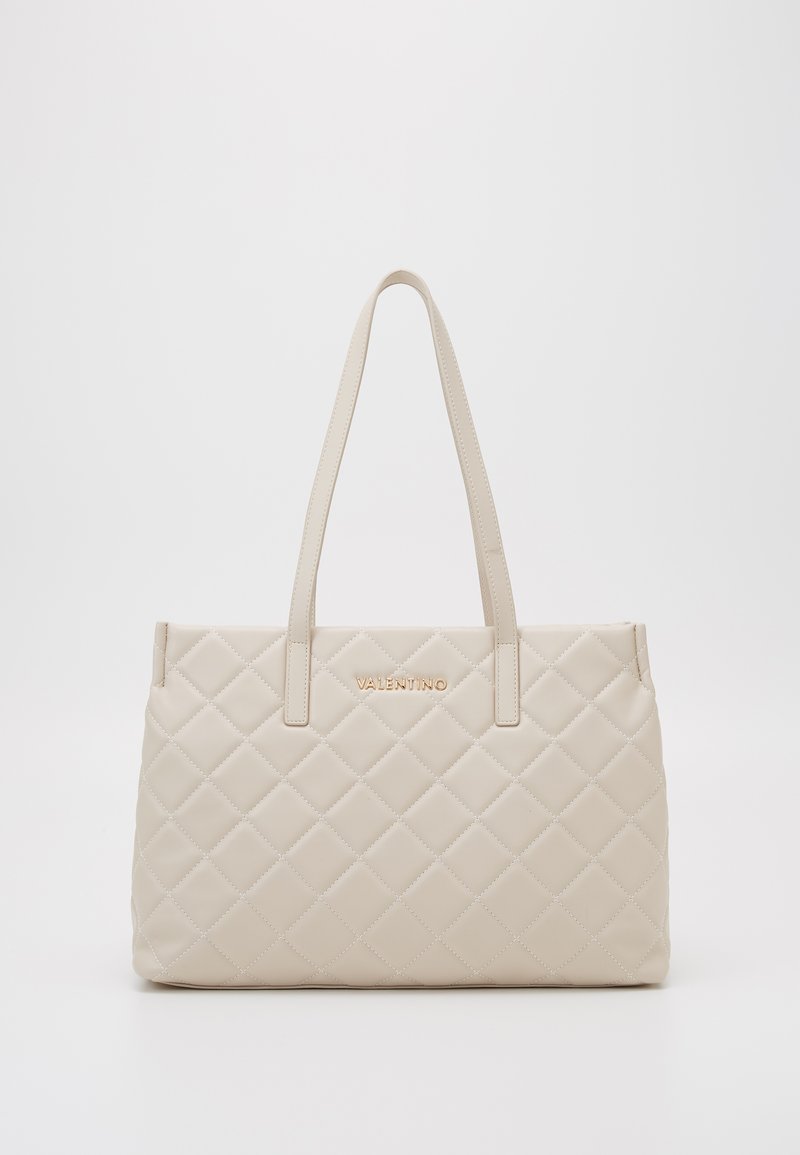 Beige, gewatteerde leren tote bag met twee handgrepen, voorzien van een gouden logo. Gladde textuur en rechthoekige vorm met een gestructureerd ontwerp.