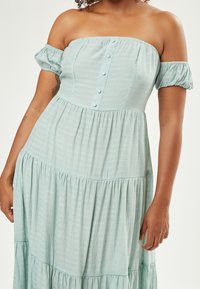 Himmelblaues, schulterfreies Kleid mit kurzen Puffärmeln, das mit Knopfdetails und schichtigem, strukturiertem Stoff versehen ist. Luftiges und lässiges Design.