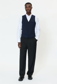 Jūras zilas vestes ar piecām melnām pogām komplektā ar baltu kreklu un melnām biksēm, kas izceļas ar ērtu piegriezumu un klasisku dizainu. Melnas kurpes.