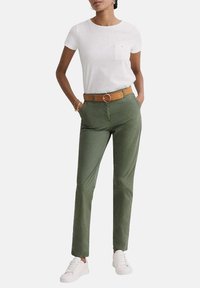T-shirt blanc à manches courtes avec une poche ; pantalon vert ajusté ; ceinture marron avec une boucle circulaire ; baskets blanches.