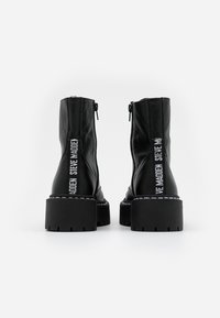 Black ankle boots made of textured leather, featuring a chunky sole and side zippers. Logo detail in white on the back.
