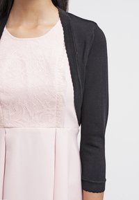 Svart stickad cardigan med trekvartsärmar lagd över en klänning i rosafärg som har en spetstopp och en veckad kjol.