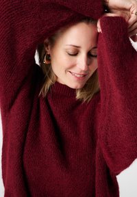 Pull en maille bordeaux avec un col montant, des manches larges et amples, et un tissu doux et texturé. Apparence chaude et confortable.