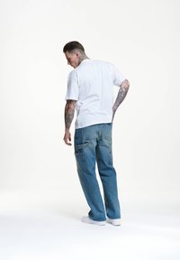Camiseta blanca de manga corta y jeans de mezclilla azul de corte holgado con bolsillos; presenta un lavado descolorido y sutiles detalles de costura.