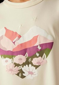 Camisa de manga corta en color crema claro con un estampado colorido de montañas y flores en rosa, púrpura y verde, con detalles bordados y una textura suave.