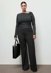 Bluză gri cu mânecă lungă și design asimetric, combinată cu pantaloni stract de talie înaltă cu dungi. Geantă tote neagră cu mânere lungi.