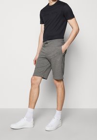 Šedé kraťasy vyrobené z měkké látky s elastickým pasem a šňůrkou, spárované s přiléhavým černým tričkem a bílými teniskami.