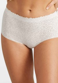 Culottes blancs en dentelle courte avec un bord festonné, présentant un motif floral texturé et une finition lisse. Tissu extensible pour le confort.