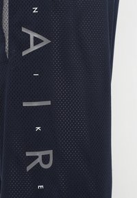 Mörkblå andningsbar mesh tyg med stora vertikala grå bokstäver och mindre vita bokstäver som stavar "AIR" och "NIKE."