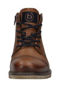 Bruine leren enkelboots met marineblauwe veters en een ronde neus. Beschikt over een blauwe patch met een logo en een gestructureerd oppervlak. Lichtgekleurde zool.