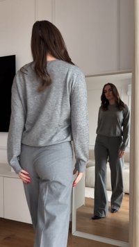 Pulover gri cu mâneci lungi, croială lejeră, asortat cu pantaloni largi gri. Textură netedă, fără modele sau accente vizibile.