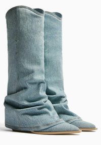 Denim-Ankleboots mit einem lässigen Design. Hellblaue Farbe, spitz zulaufende Zehenpartie und flache Sohle. Auffällige Stichdetails im Obermaterial.