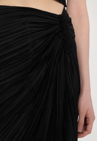 Fekete, plisszírozott szoknya, oldalán redőzéssel, sima textúrával, testhez simuló fazonra szabva.