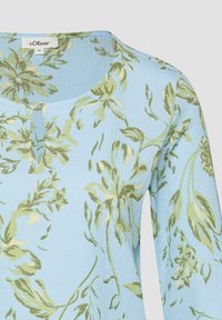 Hellblaues, strukturiertes Stoffoberteil mit grünem und beigem Blumenmuster, rundem Ausschnitt und einem einzelnen Knopfverschluss vorne.