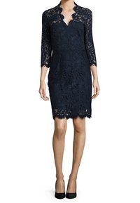 Robe en dentelle noire à mi-mollet avec un décolleté en V à bords festonnés et des manches trois-quarts, portée avec des escarpins noirs.