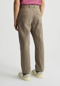 Braun gestreifte Hose mit hellrosa Nadelstreifen, ausgestattet mit zwei Gesäßtaschen. Kombiniert mit weißen Sneakers und einem lässigen Schnitt.