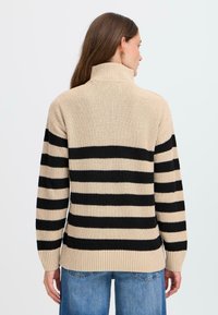 Beige und schwarz gestreifter Pullover mit hohem Kragen, gerippter Textur und lockerer Passform, der horizontale Streifen über den Rücken aufweist.