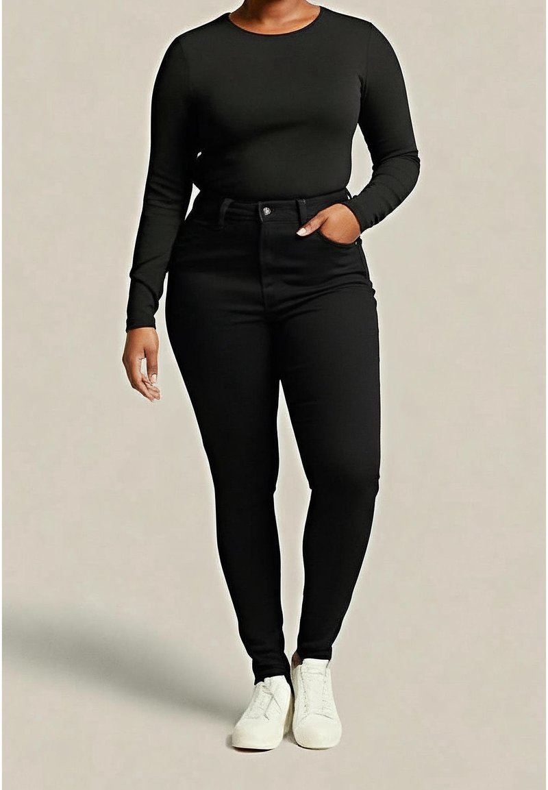Personne portant un haut noir ajusté à manches longues, un pantalon noir taille haute et des baskets blanches, debout avec une main dans la poche.