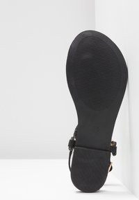 Zwarte sandaal met een gestructureerde rubberen zool, voorzien van een gevlochten bandontwerp en een glad voetbed. De hak is plat met minimale hardware.