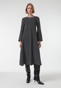 Vestido de chevron en blanco y negro con mangas largas, silueta en A, tejido texturizado, combinado con botas altas negras.