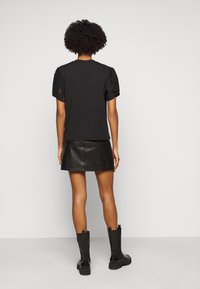 Camiseta negra con mangas de encaje abullonadas, combinada con una falda mini de cuero y botas de tobillo negras. Diseño simple y moderno sin estampados.