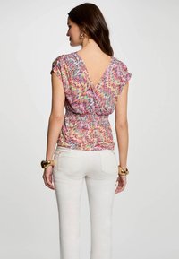 Chemise à motif zigzag coloré avec un décolleté en V profond, taille froncée et manches courtes, associée à un jean blanc ajusté. Texture de tissu lisse.
