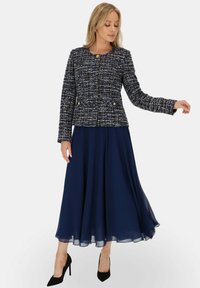 Marynarski żakiet z tweedu o teksturowanym wzorze i złotymi guzikami, w zestawieniu z zwiewną granatową spódnicą z szifonu, noszony z czarnymi szpilkami.