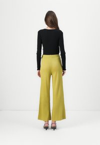 Top a maniche lunghe nero a coste abbinato a pantaloni gialli a gamba larga. I pantaloni presentano una finitura testurizzata e una vita aderente.