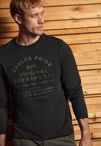 Musta pitkähihaisuus paita, jossa on haalistunut graafinen kuvio tekstillä. Kangas vaikuttaa pehmeältä ja malli on rento.