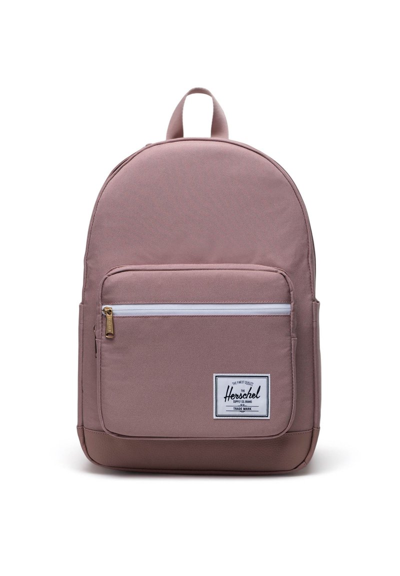 Pink fabric backpack with a rounded shape, featuring a front zip pocket, white zipper accent, and a textured lower base. Herschel logo patch included.