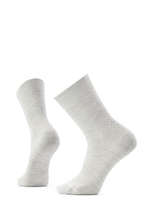 Par de calcetines blancos hasta media pantorrilla con un patrón de punto texturizado tipo panal, colocados como si estuvieran puestos en los pies sobre un fondo blanco.