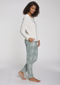 Haut à manches longues de couleur crème avec un col rond, associé à un pantalon vert à motifs avec des rayures verticales et une texture douce.